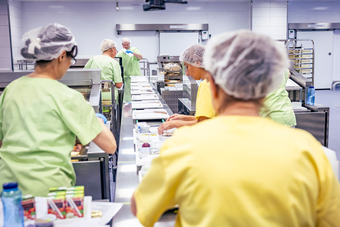 An den insgesamt vier Bändern wird das zubereitete Essen von mehreren Mitarbeitenden im Kochhaus portioniert.